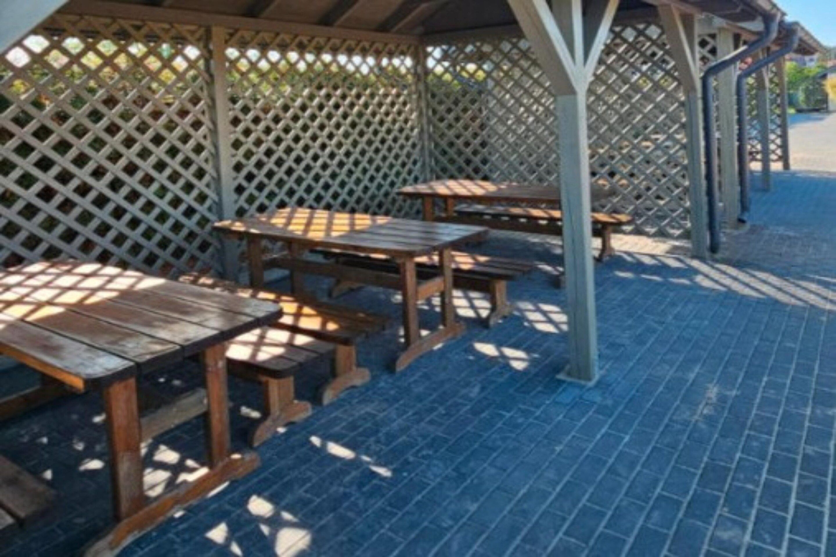 Un espace extérieur aménagé en terrasse, avec des tables et des bancs en bois, délimité par une clôture en treillis.