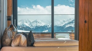 A bedroom with a bed, pillows, and a bedside table. A large window offers a view of snow-capped mountains. - Apartment in Kaltenbach With Ski-in Access (Kaltenbach)