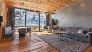 A modern living room with a wooden ceiling, large windows with a snowy mountain view, a grey sofa, a coffee table, and a rug. - Apartment in Kaltenbach With Ski-in Access (Kaltenbach)