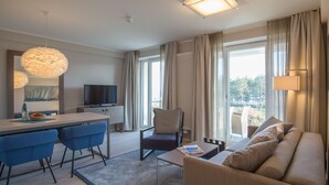 A modern hotel room with a dining area, a sofa, a chair, a television, and large windows. - Dunenresidenz Prora (Binz)