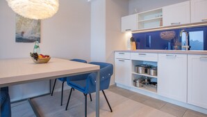 A modern kitchen with white cabinets, a blue countertop, and a dining area with a table and chairs. - Dunenresidenz Prora (Binz)