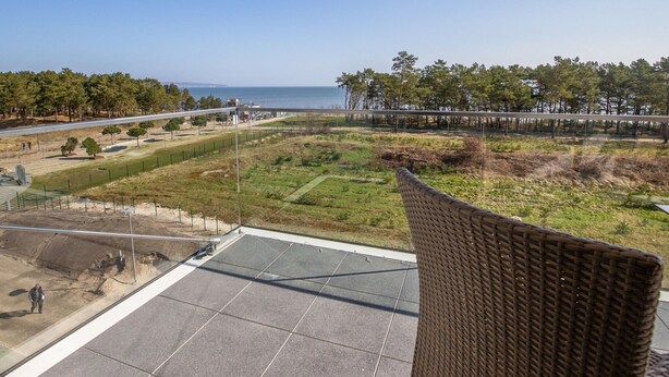 A balcony with a view of a coastal area, including a road, trees, and a body of water. - Dunenresidenz Prora (Binz)