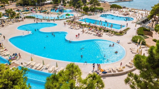 A large outdoor swimming pool with multiple sections, surrounded by sun loungers and umbrellas, with a view of the sea. - Zaton Apartment Near Sea Beach (Nin)