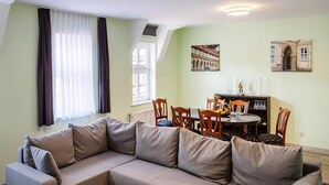 A living room with a beige sectional sofa, a dining table with chairs, and a small white table. - Ferienwohnung Schlossblick, Wernigerode (Wernigerode)