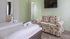 A hotel room with two beds, a floral sofa, a TV mounted on the wall, and a door leading to another room. - Ferienwohnung Schlossblick, Wernigerode (Wernigerode)