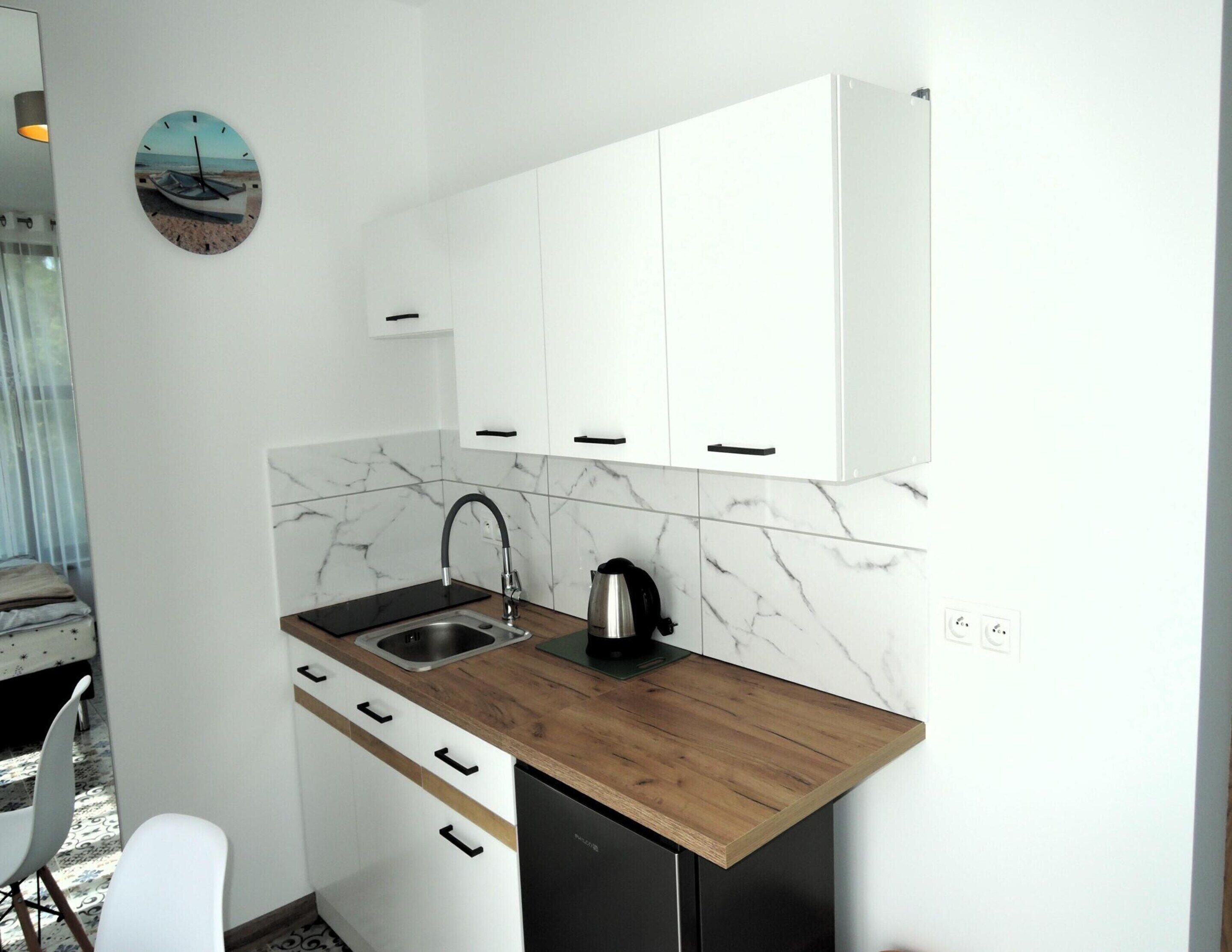 Eine kleine Küche mit weißen Schränken, einer Holz Arbeitsplatte, einem Spülbecken und einem Wasserkocher.