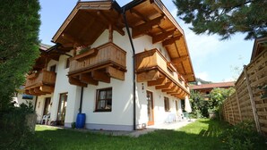 A two-story chalet with wooden balconies, a white exterior, and a well-maintained garden. - Apartment in Bramberg Near Ski Lift & Wildkogel (Bramberg am Wildkogel)