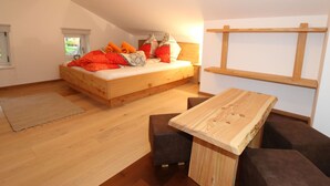 A bedroom with a wooden bed, a wooden table, and a sloped ceiling. - Apartment in Bramberg Near Ski Lift & Wildkogel (Bramberg am Wildkogel)