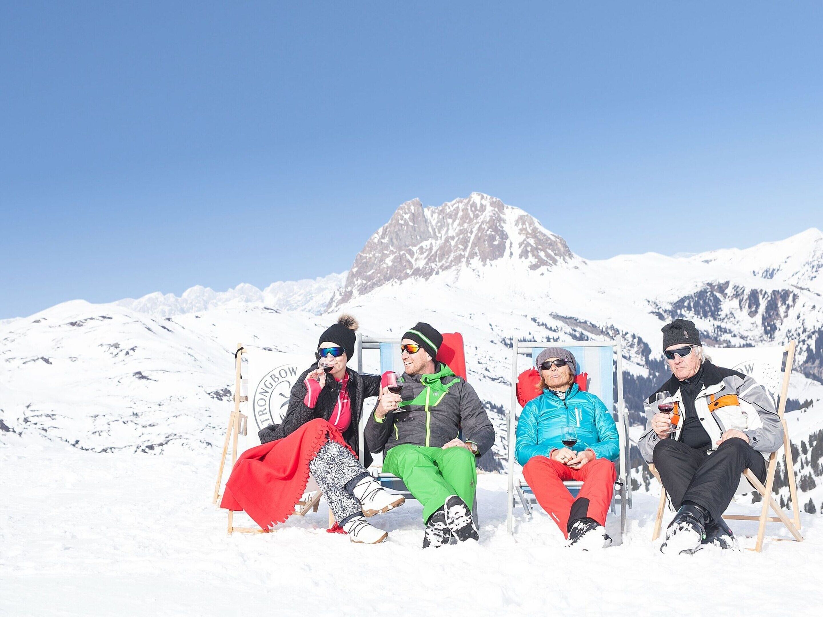 Four people sitting on chairs in a snowy outdoor setting with a mountain in the background.