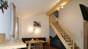 A dining area with a wooden table, chairs, and a sofa. There is a staircase with wooden railings leading to an upper level. - Apartment in Bramberg Near Ski Lift & Wildkogel (Bramberg am Wildkogel)