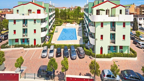 A modern apartment building with a central swimming pool, multiple balconies, and a parking area. - Apartment in Caorle With Heating (Caorle)