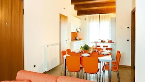 A dining area with a wooden ceiling, orange chairs, and a white table. - Apartment in Caorle With Heating (Caorle)