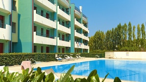 A multi-story hotel with a swimming pool, surrounded by greenery and trees. - Apartment in Caorle With Heating (Caorle)