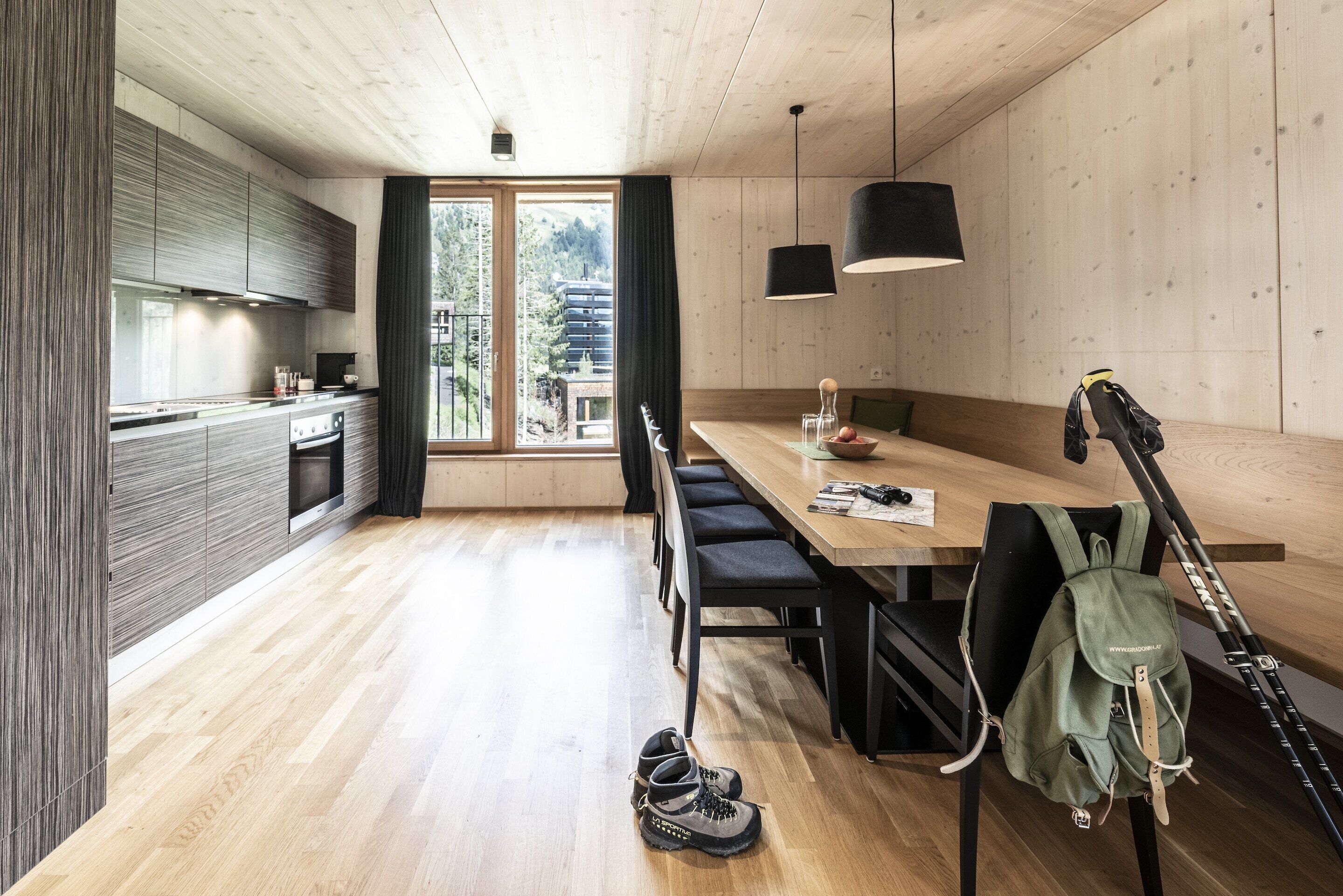 A modern kitchen with wooden cabinets and a large window. There is a dining table with chairs and a backpack on it.