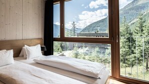 Un dormitorio con un ventanal grande, paredes de madera y una cama con ropa de cama blanca.