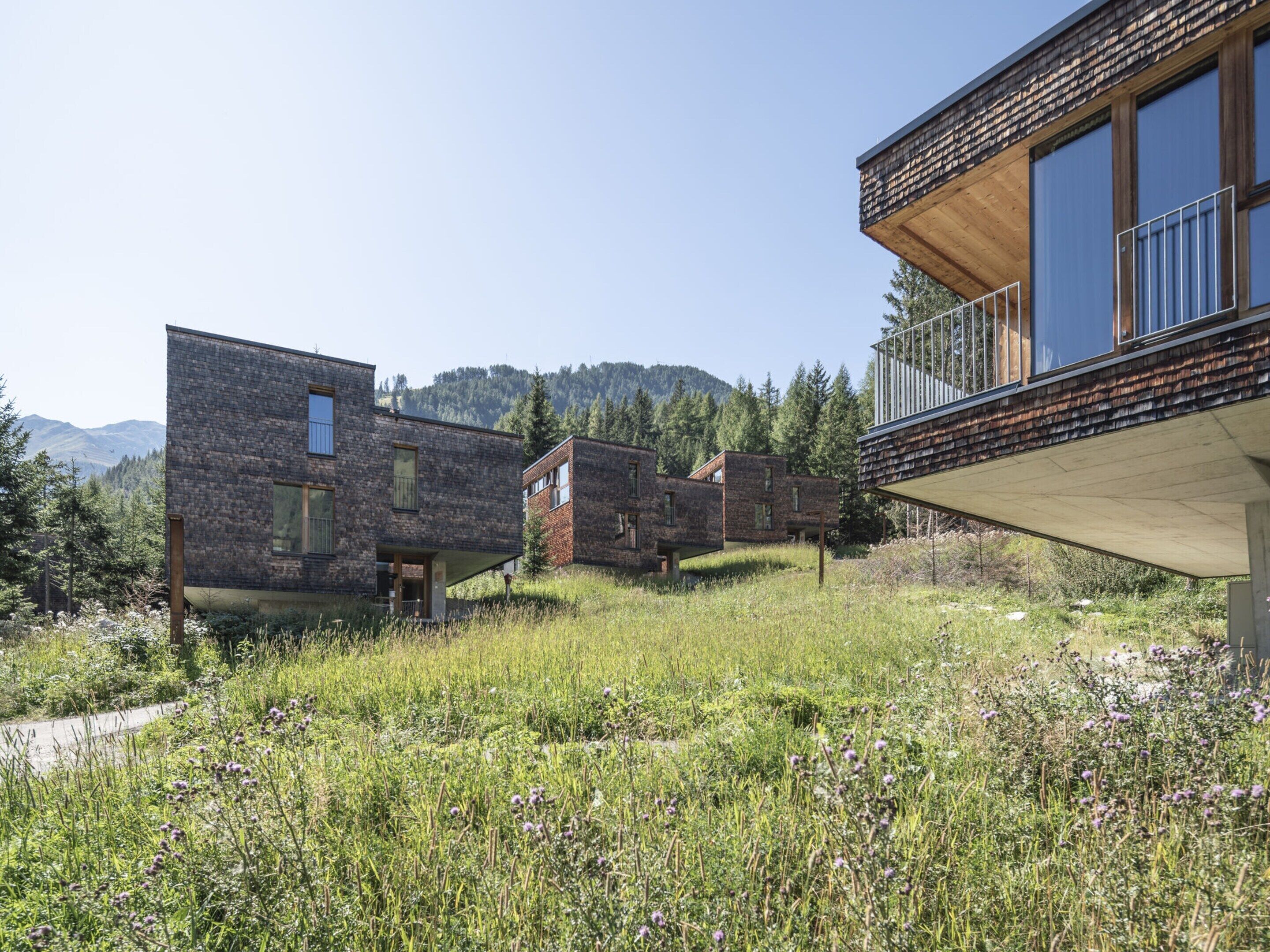 A modern building with a flat roof and large windows, surrounded by a grassy field and trees.