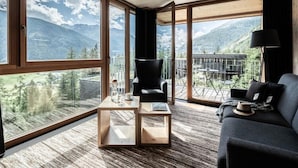 Un moderno salón con ventanas amplias que ofrecen vistas a las montañas, un sillón de cuero negro, un sofá oscuro y una mesa de centro de madera.