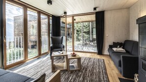 Una sala de estar moderna con ventanas amplias, un sofá negro, una mesa de centro de madera y un sillón negro.