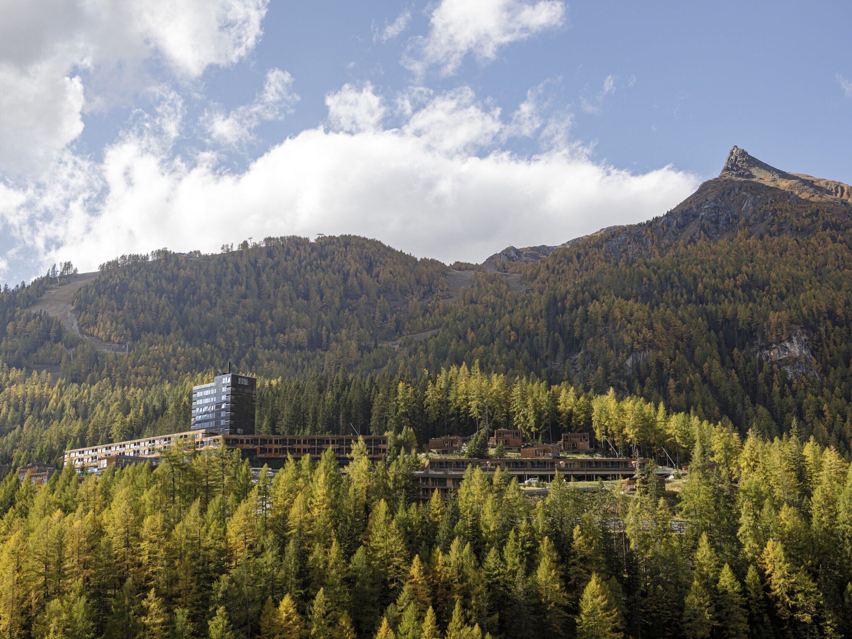 Un hotel con varias construcciones ubicado entre colinas boscosas, con vistas al paisaje montañoso circundante.