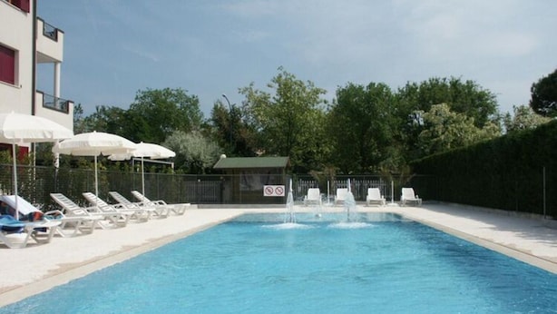 A swimming pool with lounge chairs and umbrellas, surrounded by a fence and trees. - Residence Vecchio Faro in Cavallino-treporti-formerly TUI Ferienhaus (Cavallino-Treporti)