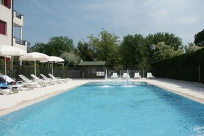 Una piscina con sillas de descanso y sombrillas, rodeada por una valla y árboles.