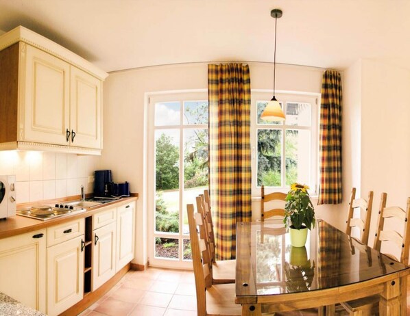 A kitchen with white cabinets, a wooden dining table, and a large window with plaid curtains. - Reihenhaus im Hasseroder Ferienpark, Wernigerode (Wernigerode)