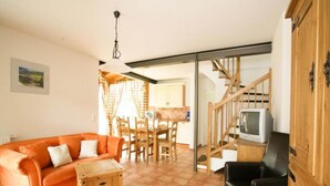 Een woonkamer met een bank, een bijzettafeltje, een televisie en een trap naar een andere kamer.