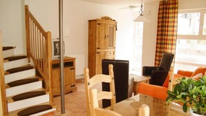 Een woonkamer met een houten trap, een eettafel met stoelen, een televisie en een kast.
