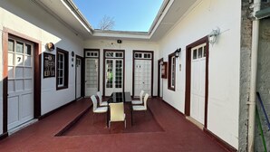 Un espacio al aire libre cubierto con una mesa y sillas, suelo de baldosas rojas y puertas blancas numeradas 7, 12 y 5.