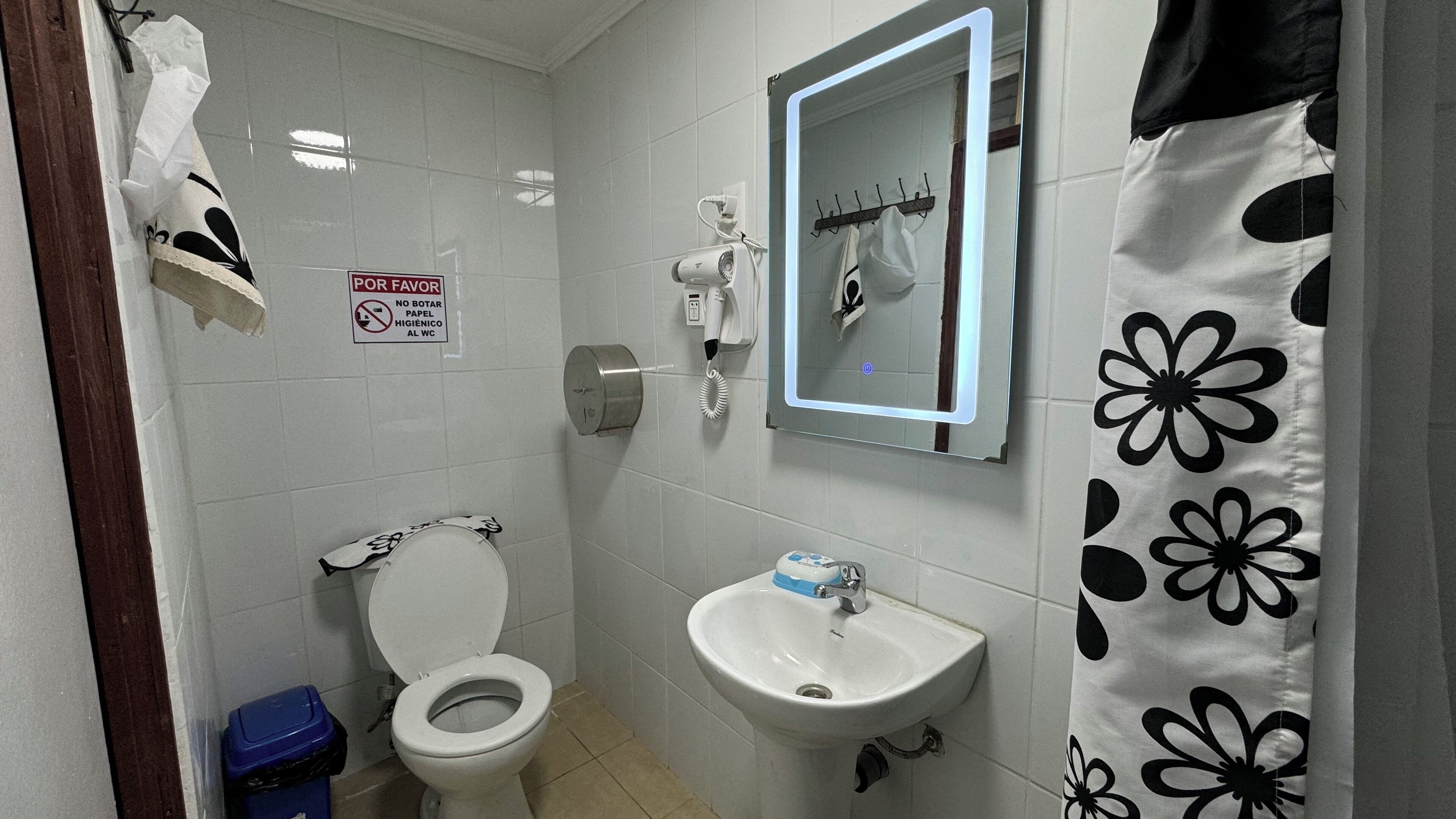 A bathroom with a toilet, sink, and a mirror with a light. There's a sign prohibiting paper towels.