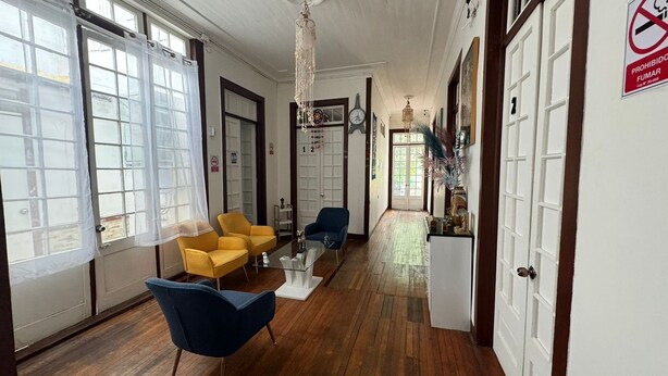 Un pasillo con suelo de madera, sillas amarillas y azules, una mesa de centro de vidrio y un armario blanco.