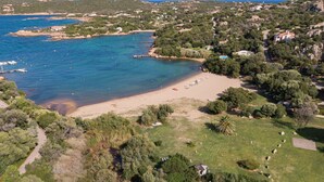 An aerial view of a coastal area with a beach, boats, and residential buildings. - Stay in Porto Cervo With Garden Setting (Arzachena)