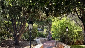 A stone pathway with lamp posts, surrounded by lush greenery and trees. - Stay in Porto Cervo With Garden Setting (Arzachena)