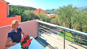 Un balcon avec une balustrade, une table et un pot de fleurs aux fleurs rouges.