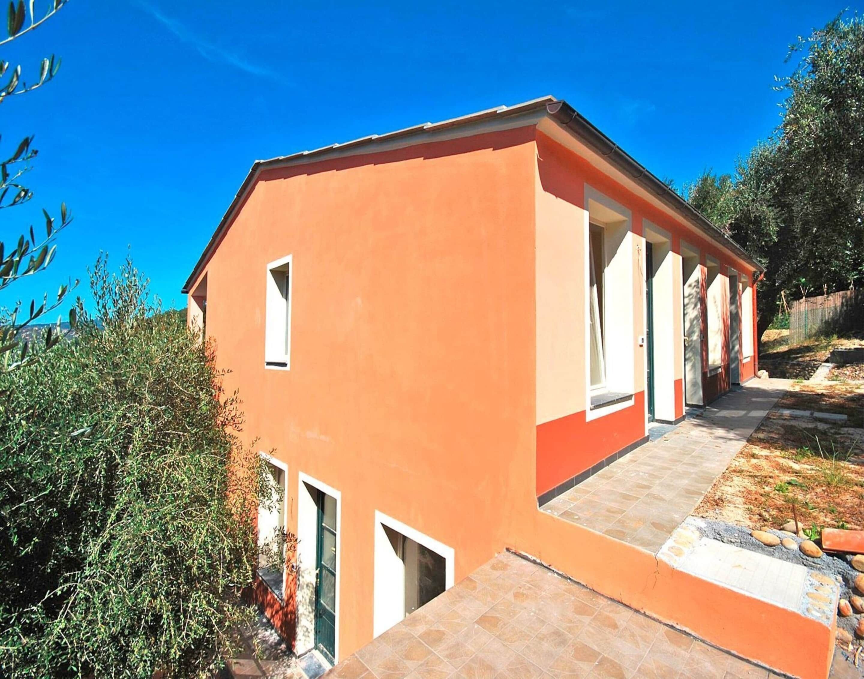 A two-story building with a red exterior, a tiled entrance, and a small garden area.