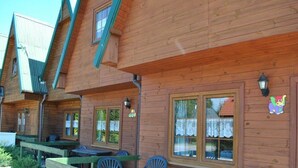 A wooden cabin with multiple windows, outdoor seating, and a small table. - Two-story Wooden Houses Close to the Beach (Mielno)
