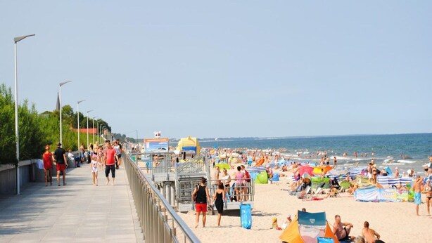 A beach with a walkway, umbrellas, and people. - Two-story Wooden Houses Close to the Beach (Mielno)