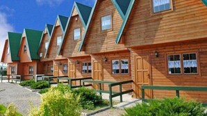 A row of wooden cabins with pitched roofs and windows, arranged in a linear fashion. - Two-story Wooden Houses Close to the Beach (Mielno)