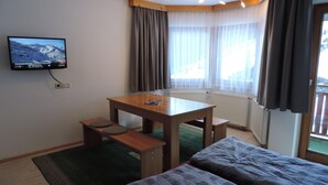 Ett hotellrum med en säng, ett skrivbord med en stol, en tv som är monterad på väggen och ett fönster med gardiner.