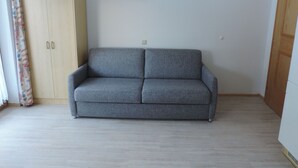 Ett rum med en grå soffa, en trägarderob och en enkel vägg med en ljusströmbrytare.