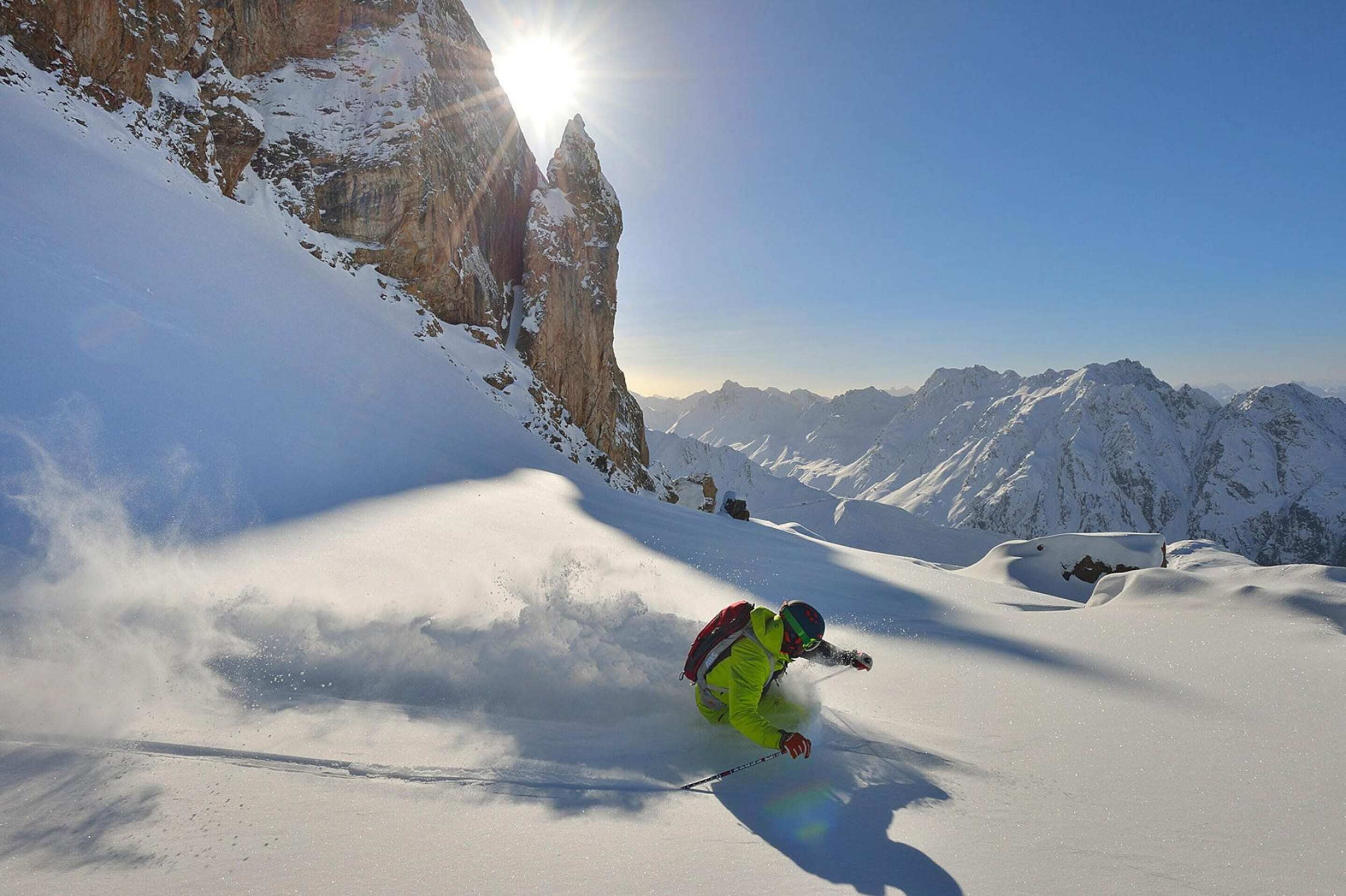 Een skiër op een besneeuwde helling, met bergen op de achtergrond.