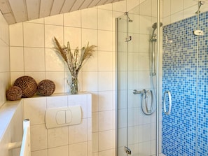 Une salle de bain avec une douche, un mur recouvert de carreaux blancs et un mur de douche orné d’une mosaïque bleue.
