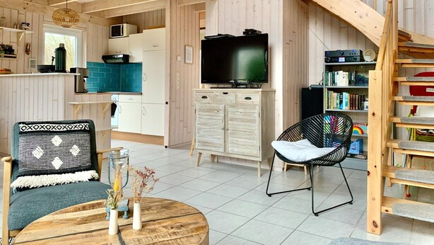 A spacious living area with a wooden staircase, a television, and a bookshelf. - Holiday Home Seeblick With Sauna on Lake Dummer, Dummer (Dümmer)