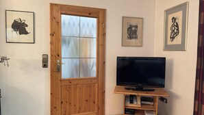 Ein Zimmer mit Holztür, einem Fernseher auf einem Holzschrank und drei gerahmten Bildern an der Wand.