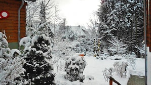Ein verschneiter Garten mit einem Holzgebäude, schneebedeckten Bäumen und einem Ziegelweg.