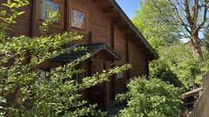 Eine Holzhütte mit geneigtem Dach, großen Fenstern und üppiger, umgebender Natur.