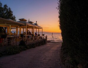Een restaurant aan zee met terras, uitkijkend op de oceaan tijdens de zonsondergang.