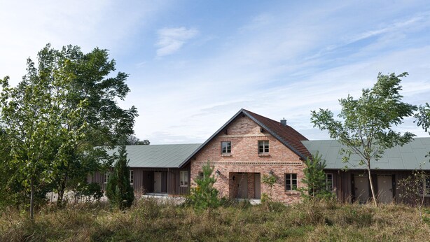 A two-story brick building with a sloped roof, surrounded by trees and grass. - Ferienwohnung mit Kamin im Gut Ulrichshusen (Moltzow)