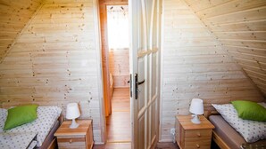 A cozy attic bedroom with two wooden beds, each with a nightstand and a lamp. A door leads to an adjacent room. - Holiday Home in Przewloka Near Baltic Beach (Ustka)