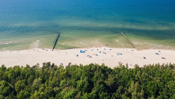 A beach with clear blue water, a sandy shore, and a forested area in the foreground. - Holiday Home in Przewloka Near Baltic Beach (Ustka)
